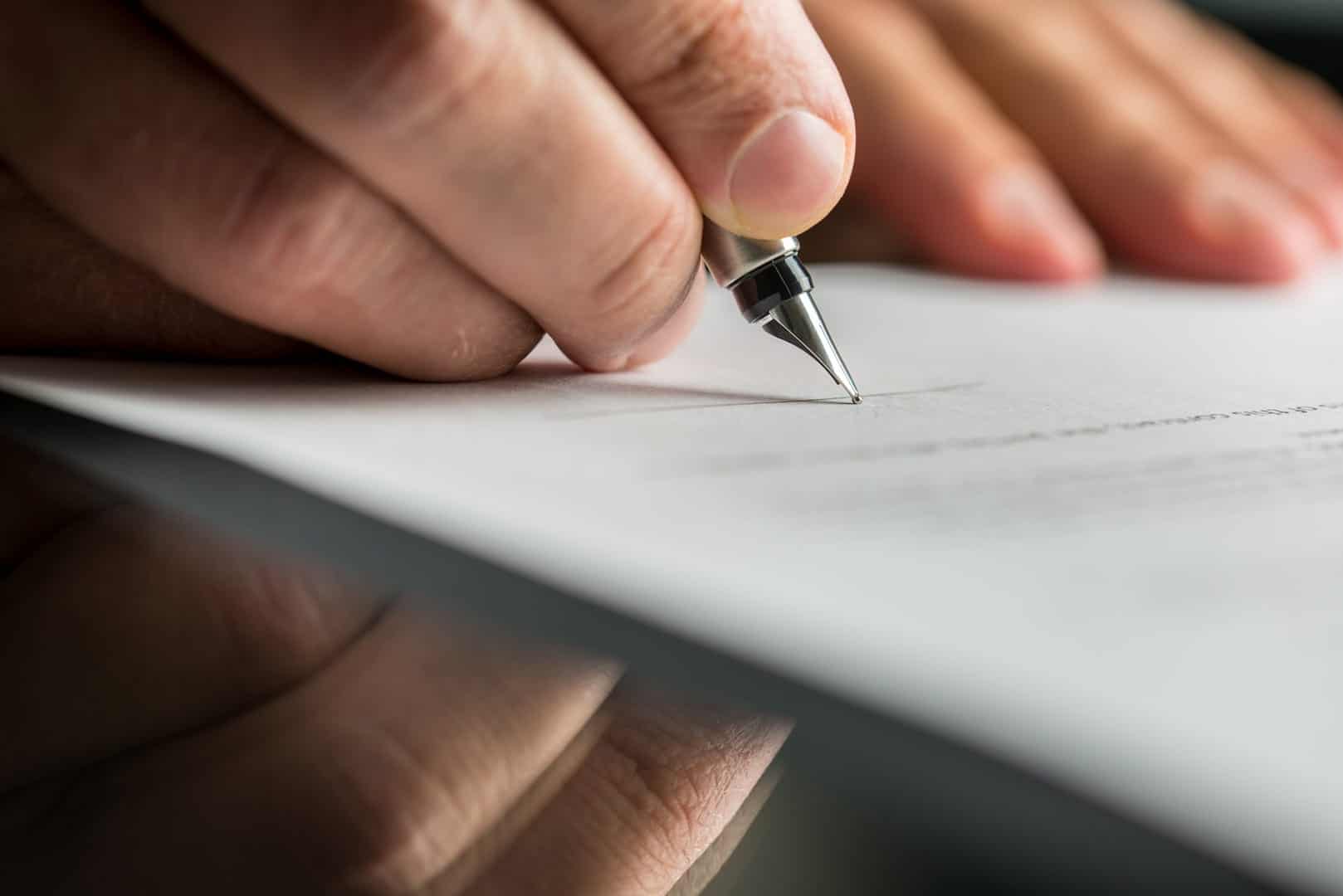 Fingers are holding a fountain pen, which is touching a piece of paper with printed text on it